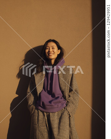 Joyful Asian woman in long coat and purple hoodie, radiating warmth and happiness under sun. Her eyes are smiling and her face is glow Joyful Asian woman in long coat and purple hoodie, radiating warmth and happiness under sun. Her eyes are smiling and her face is glow 129429951