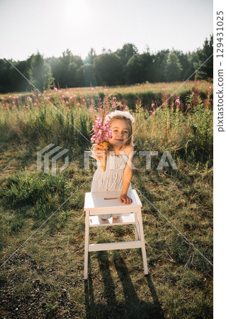 Young girl holding flowers in a sunny field during summer afternoon Young girl holding flowers in a sunny field during summer afternoon 129431025