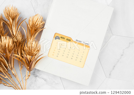 November 2026 calendar on monthly planner book with golden flower on white marble background. 129432000