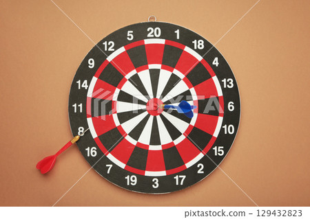 Dart board with two darts on brown background. 129432823