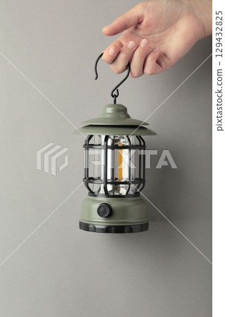 Hand holding lantern lamp on grey background. Camping. Vertical photo 129432825
