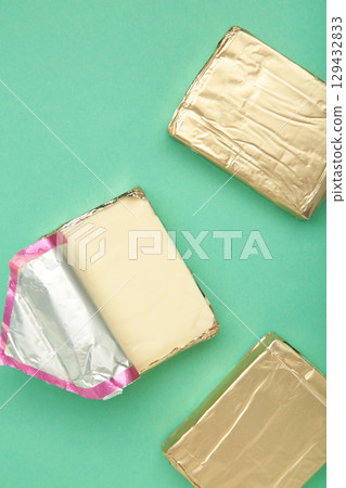 Processed cheese in foil on mint background. Vertical photo. Processed cheese in foil on mint background. Vertical photo. 129432833