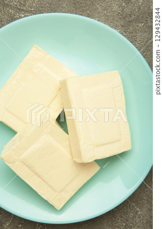 Processed cheese in foil on plate on grey concrete background Processed cheese in foil on plate on grey concrete background 129432844