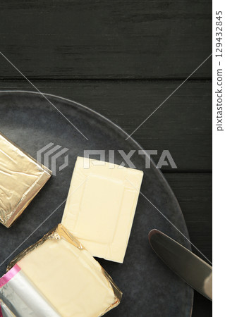 Processed cheese in foil on plate on black wooden background 129432845
