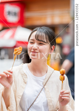 A woman eating kushikatsu (fried skewers) outdoors in Dotonbori, Osaka City, Osaka Prefecture 129433352