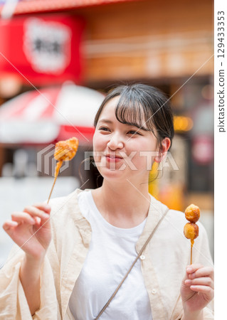 A woman eating kushikatsu (fried skewers) outdoors in Dotonbori, Osaka City, Osaka Prefecture A woman eating kushikatsu (fried skewers) outdoors in Dotonbori, Osaka City, Osaka Prefecture 129433353