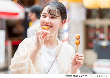 A woman eating kushikatsu (fried skewers) outdoors in Dotonbori, Osaka City, Osaka Prefecture A woman eating kushikatsu (fried skewers) outdoors in Dotonbori, Osaka City, Osaka Prefecture 129433357