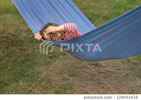 A cute funny girl with glasses is swinging on a striped hammock straightening curly disheveled hair A cute funny girl with glasses is swinging on a striped hammock straightening curly disheveled hair 129433419