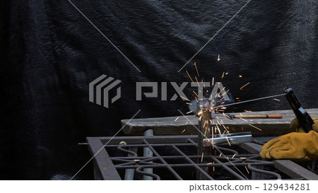 Close-up of hands in protective gloves performing arc welding on metal bars with visible sparks and smokein industrial safety and precision in metalwork fabrication 129434281