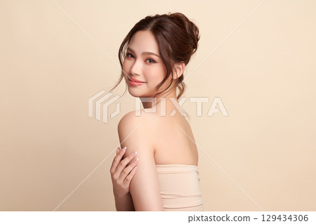 A beautiful young Asian woman with clean, fresh skin against a beige background. Skincare, facial treatment, cosmetology, beauty, and spa. An elegant portrait of an Asian woman. 129434306