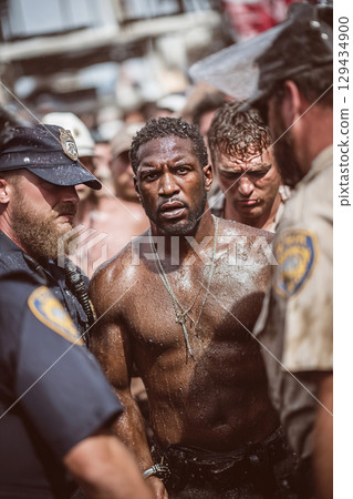 Police officers escort handcuffed suspect through crowd of upset bystanders during arrest event 129434900