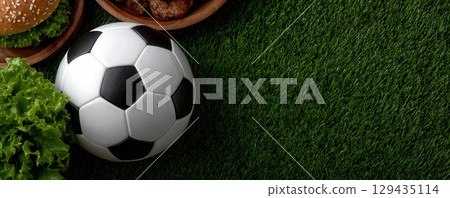 Soccer ball on green grass with burgers and lettuce, perfect for game night or sports themed gatherings 129435114
