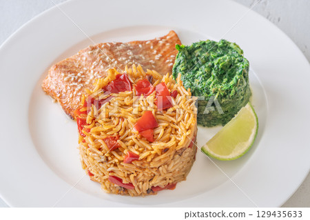 Elegant plated salmon with rice pilaf and creamy spinach on white round plate 129435633