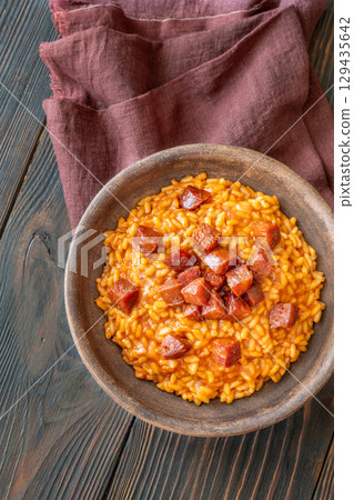 Rustic bowl of spicy tomato and chorizo risotto on wooden table 129435642