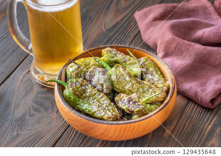 Terracotta bowl of Pimientos de Padron served with cold frothy beer 129435648