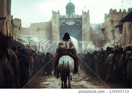 Jesus Christ enters Jerusalem on a donkey through large stone gates surrounded by crowd 129435713