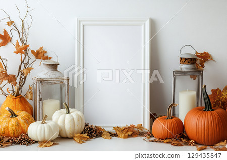 A blank, vertical black picture frame is a centerpiece surrounded by autumn decor. The decorations include pumpkins, lanterns with candles, dried leaves, and tall grasses. A blank, vertical black picture frame is a centerpiece surrounded by autumn decor. The decorations include pumpkins, lanterns with candles, dried leaves, and tall grasses. 129435847