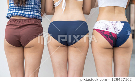 夏日海灘上三個身穿比基尼和牛仔短褲的女孩的背影，美麗的臀部和臀部 129437162