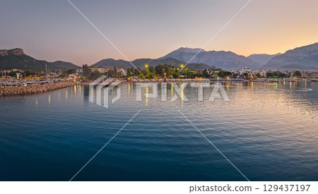 Dusk scene in Kemer, Turkey, showing the town illuminated coastline and beach, reflected beautifully on the calm sea. Majestic Taurus mountains silhouettes in the background 129437197