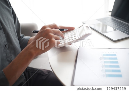 Closeup hand of businessman using calculator, laptop and reading report in office Closeup hand of businessman using calculator, laptop and reading report in office 129437239