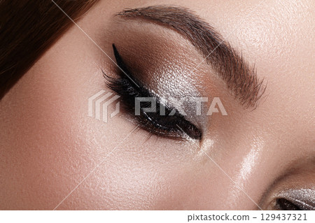 Close-up macro photograph of a female eye with elegant classic eyeliner. Well-groomed eyebrows, soft brown eyeshadow and voluminous long lashes 129437321