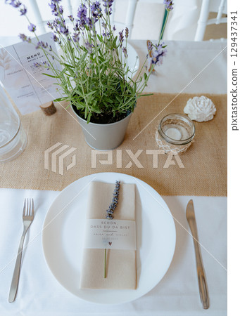 Rustic wedding table setting with lavender in a pot, folded napkin with dried lavender, and elegant menu card. Perfect for event decoration, wedding planning, and floral design Rustic wedding table setting with lavender in a pot, folded napkin with dried lavender, and elegant menu card. Perfect for event decoration, wedding planning, and floral design 129437341