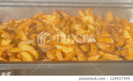 Close up of seasoned potato wedges in a buffet warmer. Warm, crispy and golden, perfect for catering, wedding menus, restaurant promotions, food blogs and commercial food photography. Close up of seasoned potato wedges in a buffet warmer. Warm, crispy and golden, perfect for catering, wedding menus, restaurant promotions, food blogs and commercial food photography. 129437344