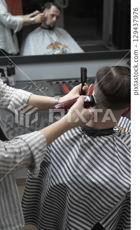 Professional barber grooming client's hair using electric clipper, delivering precise cut with skill in contemporary salon setting Professional barber grooming client's hair using electric clipper, delivering precise cut with skill in contemporary salon setting 129437976