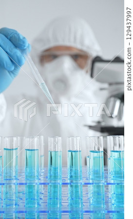 Scientific researcher wearing protective equipment, carefully pipetting liquid into test tubes while conducting medical research experiment. Medicine, healthcare and science concept Scientific researcher wearing protective equipment, carefully pipetting liquid into test tubes while conducting medical research experiment. Medicine, healthcare and science concept 129437997