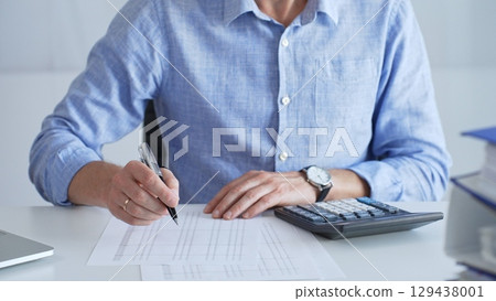 Financial professional calculating expenses, writing details next to laptop during budget analysis in corporate workspace. Audit and taxes in business 129438001