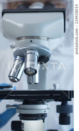 Medical virologist in a hazmat suit, mask, and gloves, diligently working at a microscope in a laboratory researching viruses. Healthcare and science concept 129438014