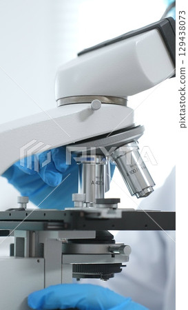 Close up of blue gloved scientist's hand adjusting microscope in modern laboratory setting. Medicine, science and health care concept 129438073
