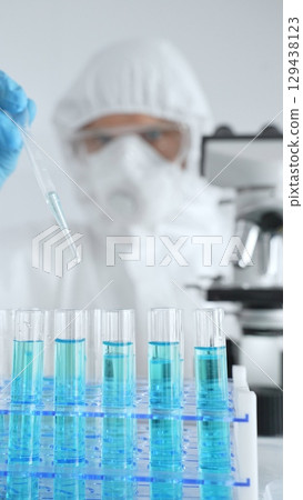 Scientific researcher wearing protective equipment, carefully pipetting liquid into test tubes while conducting medical research experiment. Medicine, healthcare and science concept Scientific researcher wearing protective equipment, carefully pipetting liquid into test tubes while conducting medical research experiment. Medicine, healthcare and science concept 129438123