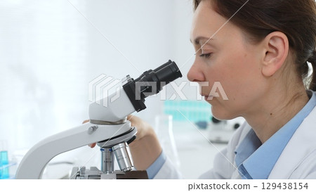 Female scientist examining samples through a microscope in a modern lab, conducting pharmaceutical research and developing treatments. Medicine, healthcare and science concept Female scientist examining samples through a microscope in a modern lab, conducting pharmaceutical research and developing treatments. Medicine, healthcare and science concept 129438154