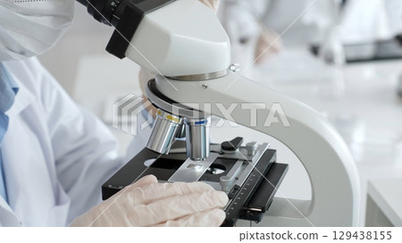 Gloved hands adjusting a microscope in a bright laboratory, emphasizing precision and focus in scientific research. Medicine, healthcare and science concept Gloved hands adjusting a microscope in a bright laboratory, emphasizing precision and focus in scientific research. Medicine, healthcare and science concept 129438155