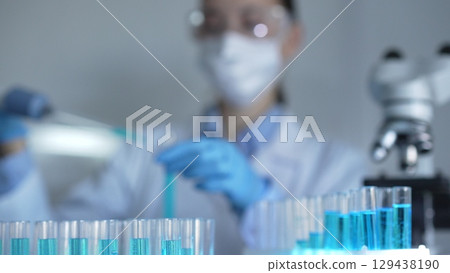 Laboratory tubes are in focus, closeup view. Female scientist researcher is using a micropipette at the background. Medicine and science Laboratory tubes are in focus, closeup view. Female scientist researcher is using a micropipette at the background. Medicine and science 129438190