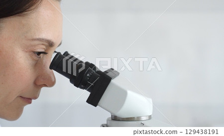 Female scientist peering into microscope, analyzing biological sample with precision in sterile laboratory research environment. Medicine and science concept Female scientist peering into microscope, analyzing biological sample with precision in sterile laboratory research environment. Medicine and science concept 129438191