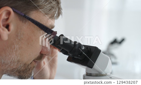 Close up of a male scientist looking through a microscope, conducting research and analysis in a laboratory setting, showcasing scientific investigation and discovery. Medicine and science concept Close up of a male scientist looking through a microscope, conducting research and analysis in a laboratory setting, showcasing scientific investigation and discovery. Medicine and science concept 129438207