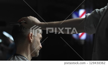 Professional barber carefully checking customer's hair texture and head contours, preparing for precise haircut, vintage barbershop interior with iconic striped pole visible Professional barber carefully checking customer's hair texture and head contours, preparing for precise haircut, vintage barbershop interior with iconic striped pole visible 129438362