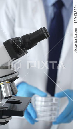 Microscope is on a table, ready for innovative medical research in a sterile laboratory environment. In the background, a scientist analyzes the data obtained. Medicine and science 129438394