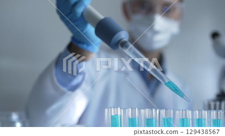 Woman scientist researcher using a micropipette to fill up test tubes with a blue liquid in laboratory setting, closeup view. Medicine and science 129438567