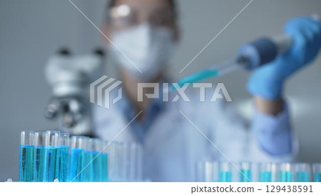 Close up of a female scientist researcher hand using a micropipette to fill up test tubes with a blue liquid in laboratory. Medicine and science 129438591