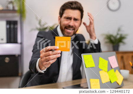 Middle-aged businessman worried by sticky notes on laptop stressed by tasks and overdue plans sighs 129440172