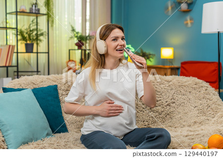 Pregnant woman dances holding smartphone like microphone joyful singing indoors with fun happy vibes Pregnant woman dances holding smartphone like microphone joyful singing indoors with fun happy vibes 129440197