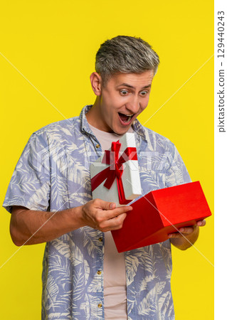 Adult man opening gift box, freezing with amazed happy face showing surprise joy unexpected present Adult man opening gift box, freezing with amazed happy face showing surprise joy unexpected present 129440243