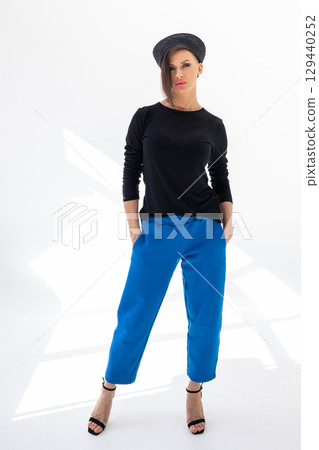 Elegant woman in black windbreaker jacket, blue pants and nautical hat on white background. Fashionable female in ocean French style. Studio photography. Vertical photo. High quality photo Elegant woman in black windbreaker jacket, blue pants and nautical hat on white background. Fashionable female in ocean French style. Studio photography. Vertical photo. High quality photo 129440252