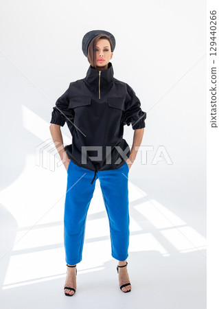 Elegant woman in black windbreaker jacket, blue pants and nautical hat on white background. Fashionable female in ocean French style. Studio photography. Vertical photo. High quality photo 129440266