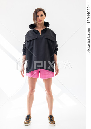 Elegant woman in black windbreaker jacket and pink shorts on light background. Fashionable female style. Studio photography. Vertical photo. High quality photo 129440304