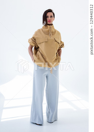 Young woman in beige windbreaker jacket and gray pants on white background. Studio photography. Vertical photo. High quality photo Young woman in beige windbreaker jacket and gray pants on white background. Studio photography. Vertical photo. High quality photo 129440312