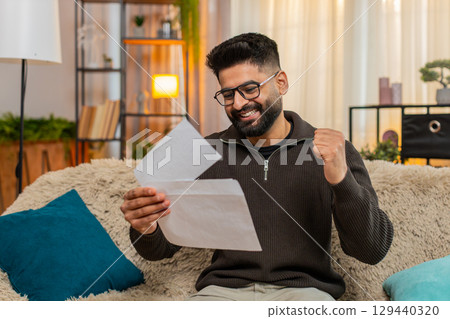 Indian man on sofa opens envelope and celebrates good news after reading positive letter at home Indian man on sofa opens envelope and celebrates good news after reading positive letter at home 129440320
